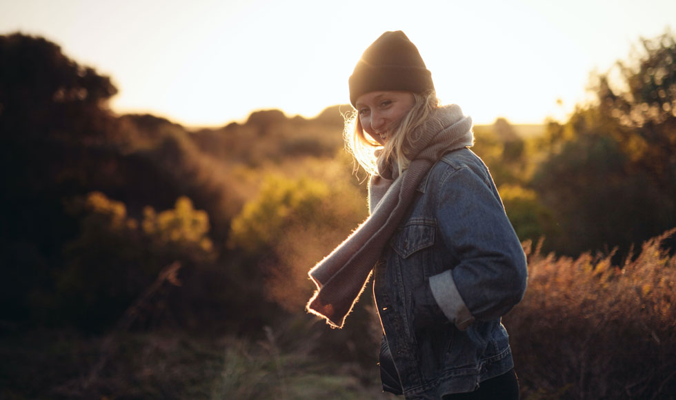 Young woman standing in a field outside at sunrise in cold weather