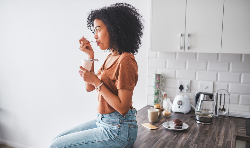 Young woman sitting on the kitcen bench eating yoghurt
