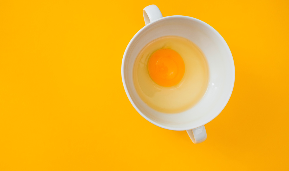 Raw egg in a white mug on a yellow background