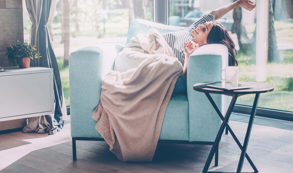 Young woman stretching out hands and smiling while lying in a big comfortable chair at home